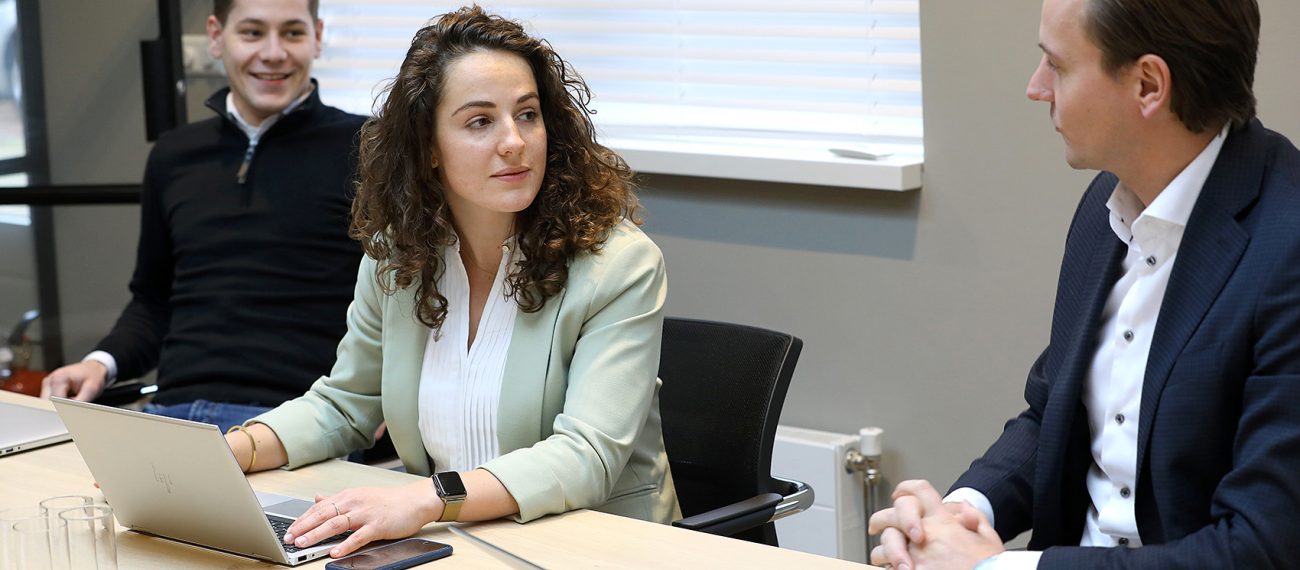 Drie collega’s zitten aan een vergadertafel met laptops en praten met elkaar tijdens een werkoverleg.