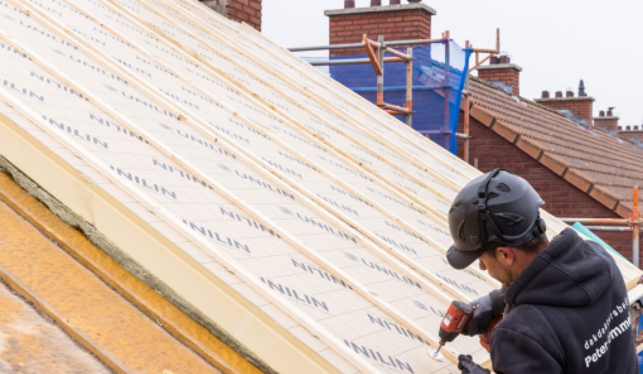 Vakman met schroefmachine monteert isolatie op hellend dak – project 91 woningen Maastricht