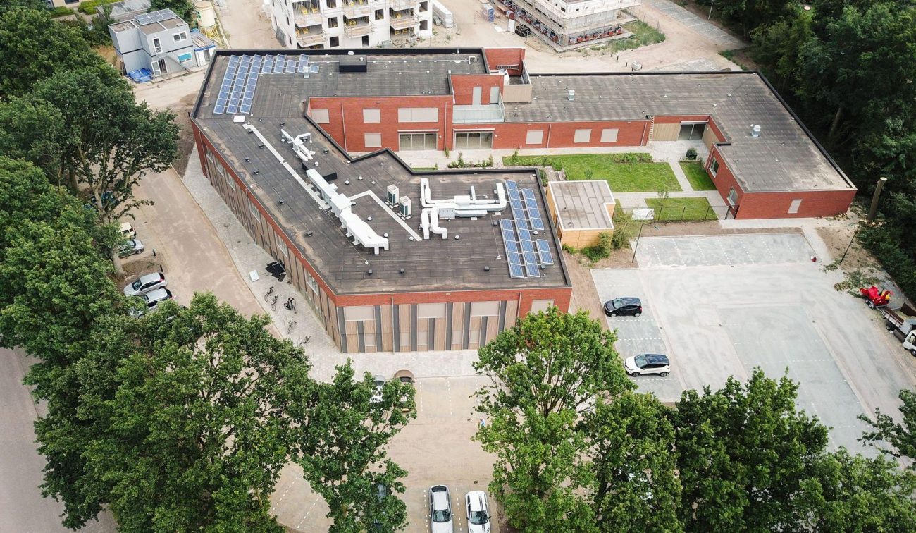 Luchtfoto van het nieuwbouwproject met het GZC en de zorgwoningen, waarop de gebouwen en omliggende groene buitenruimte zichtbaar zijn.
