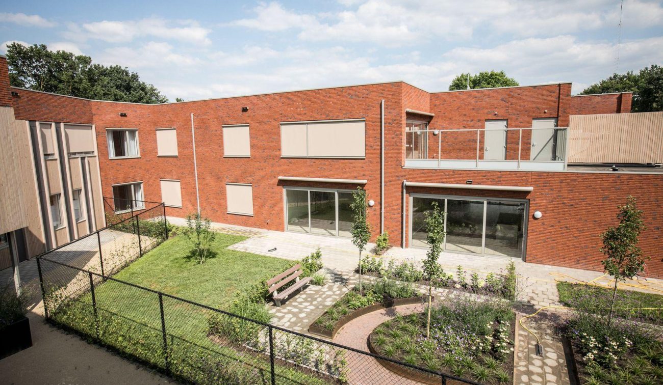 Tuin van het nieuwbouwproject met het GZC en de zorgwoningen, met groene beplanting en buitenruimte voor bewoners.