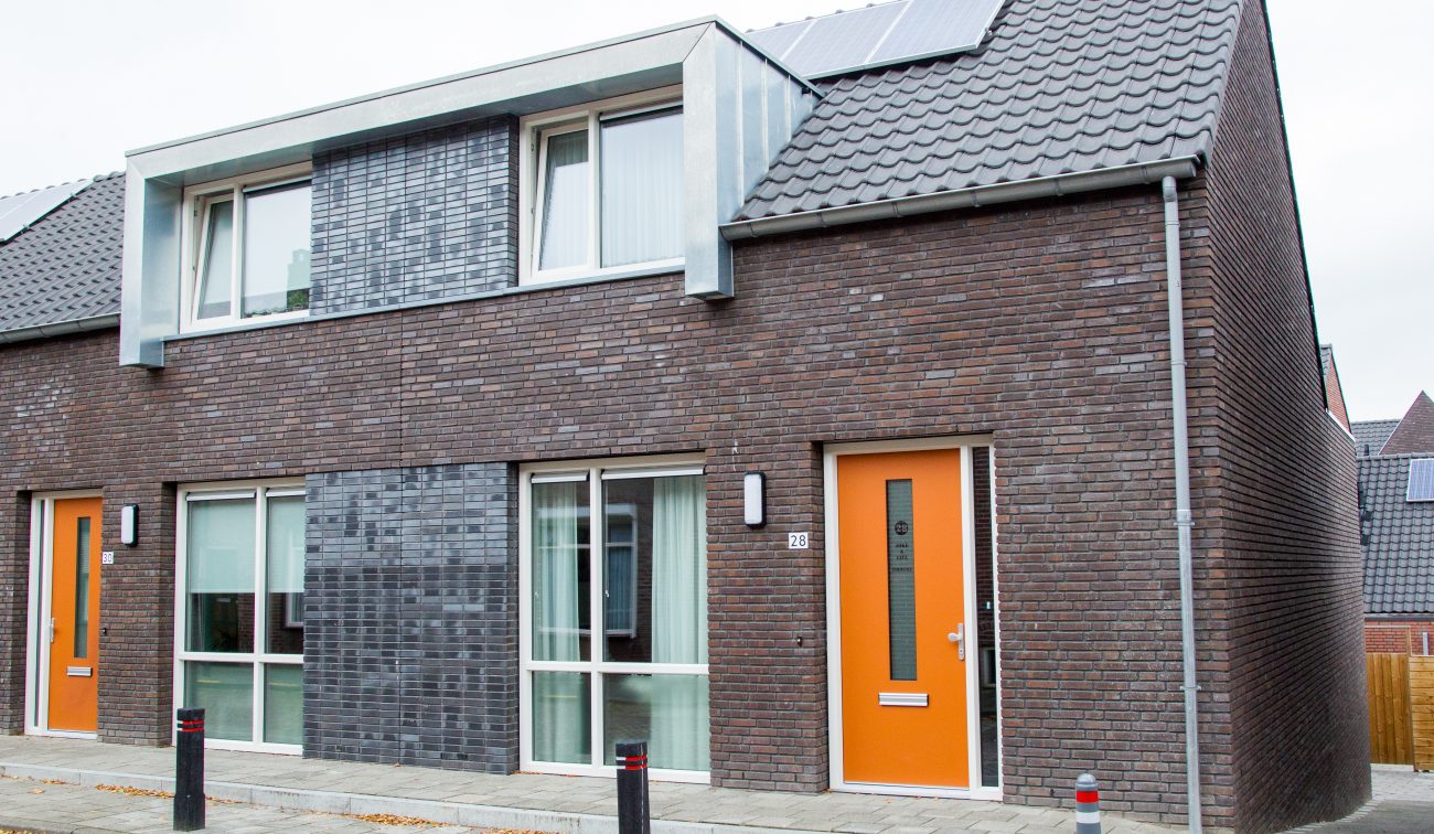 Nieuwbouwwoningen in Zevenbergen met rode en donkergrijze bakstenen gevels, opvallende oranje voordeuren en moderne zinken dakkapellen