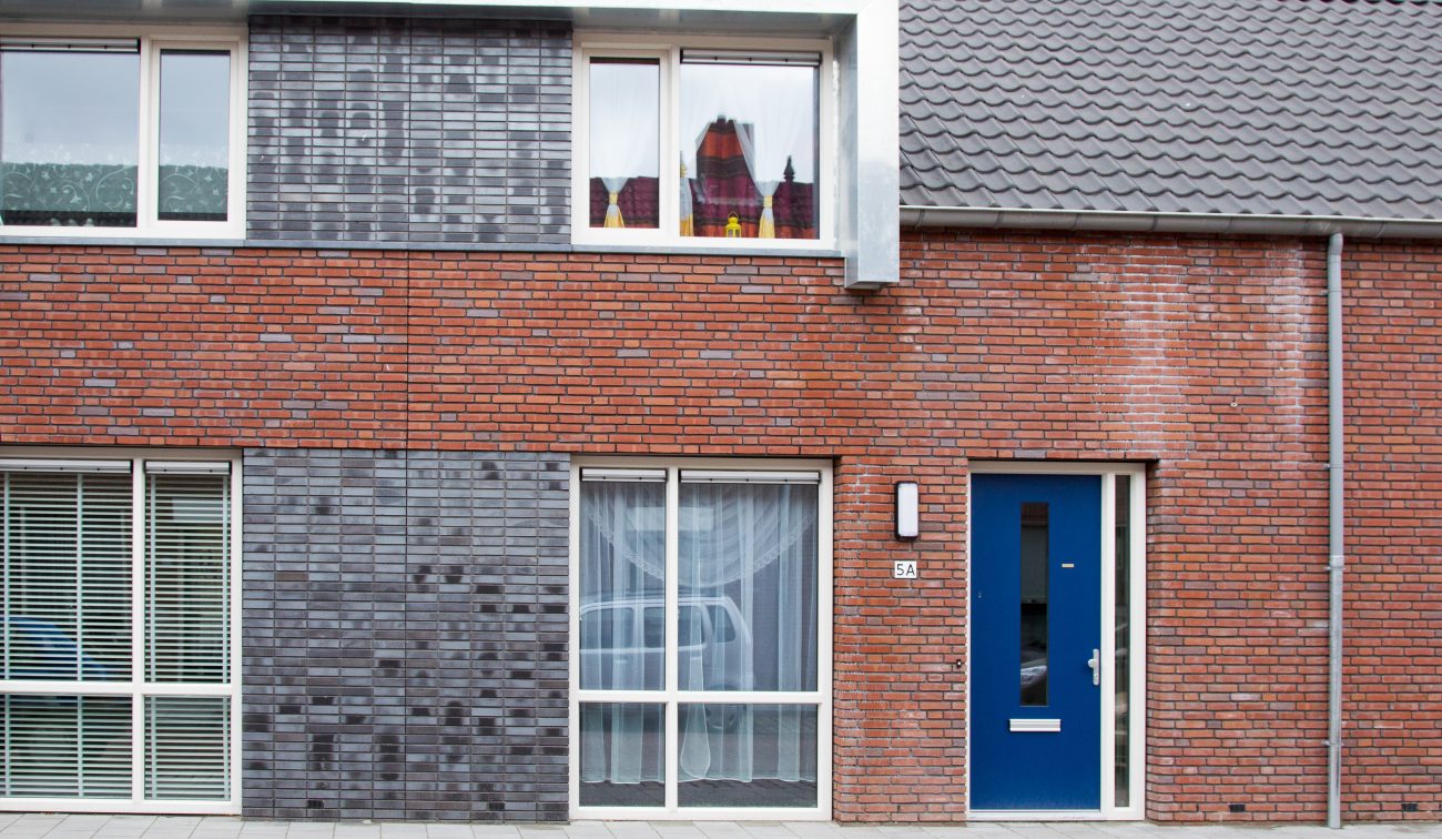 Nieuwbouwwoning in Zevenbergen met moderne baksteenarchitectuur, rode en donkergrijze gevelstenen, witte kozijnen en een opvallende blauwe voordeur.