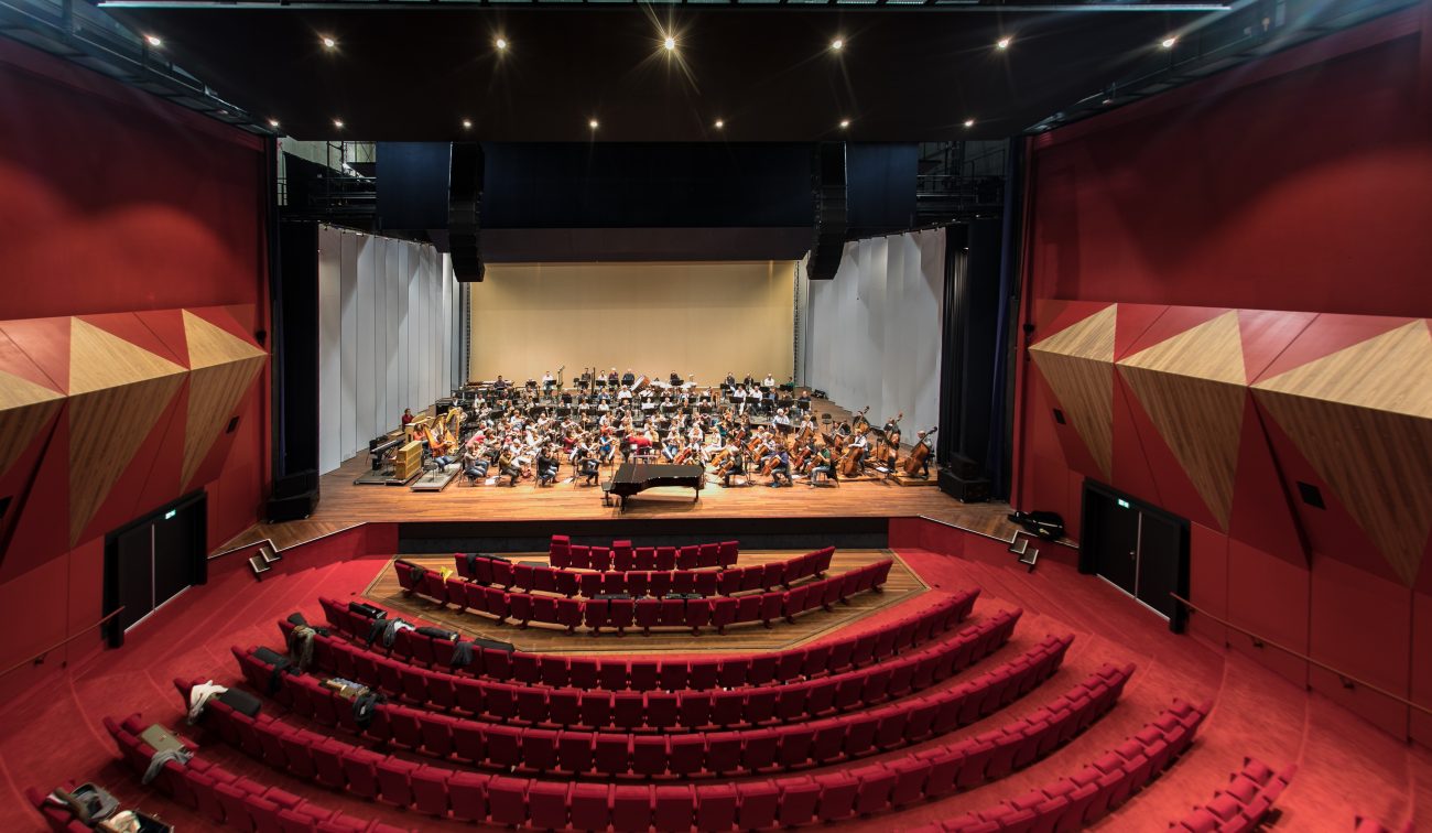 Panorama theater Vrijthof Maastricht: gebogen rijen stoelen, breed podium en repeterend orkest