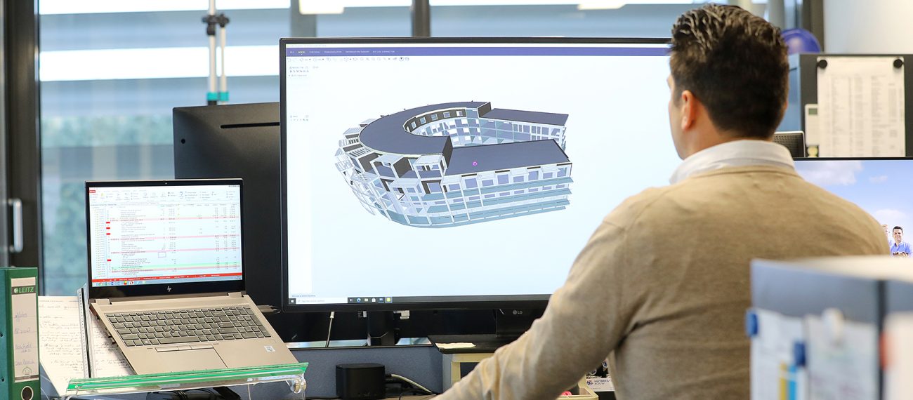 Medewerker werkt aan 3D-gebouwmodel in BIM-software op groot scherm in moderne kantooromgeving.