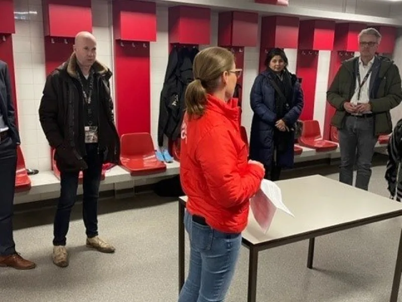 Rondleiding door kleedkamer met rode lockers en bezoekers rond een gids