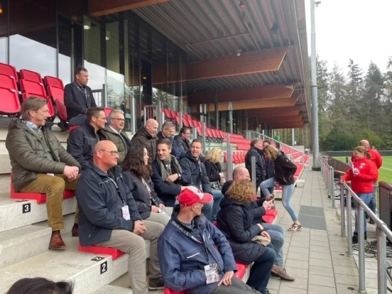 Groep bezoekers zit op rode tribune tijdens rondleiding bij sportcomplex