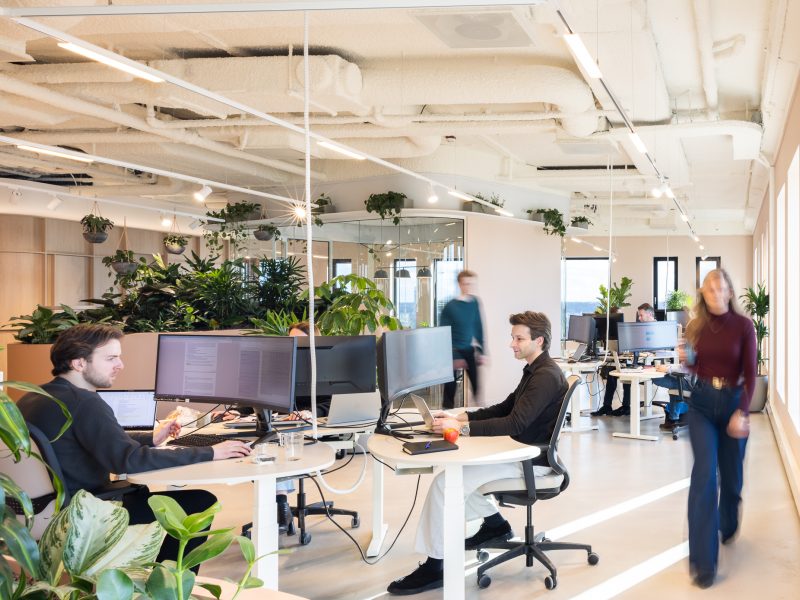 Moderne kantoorruimte met veel planten waar medewerkers werken aan bureaus in een licht en open interieur.