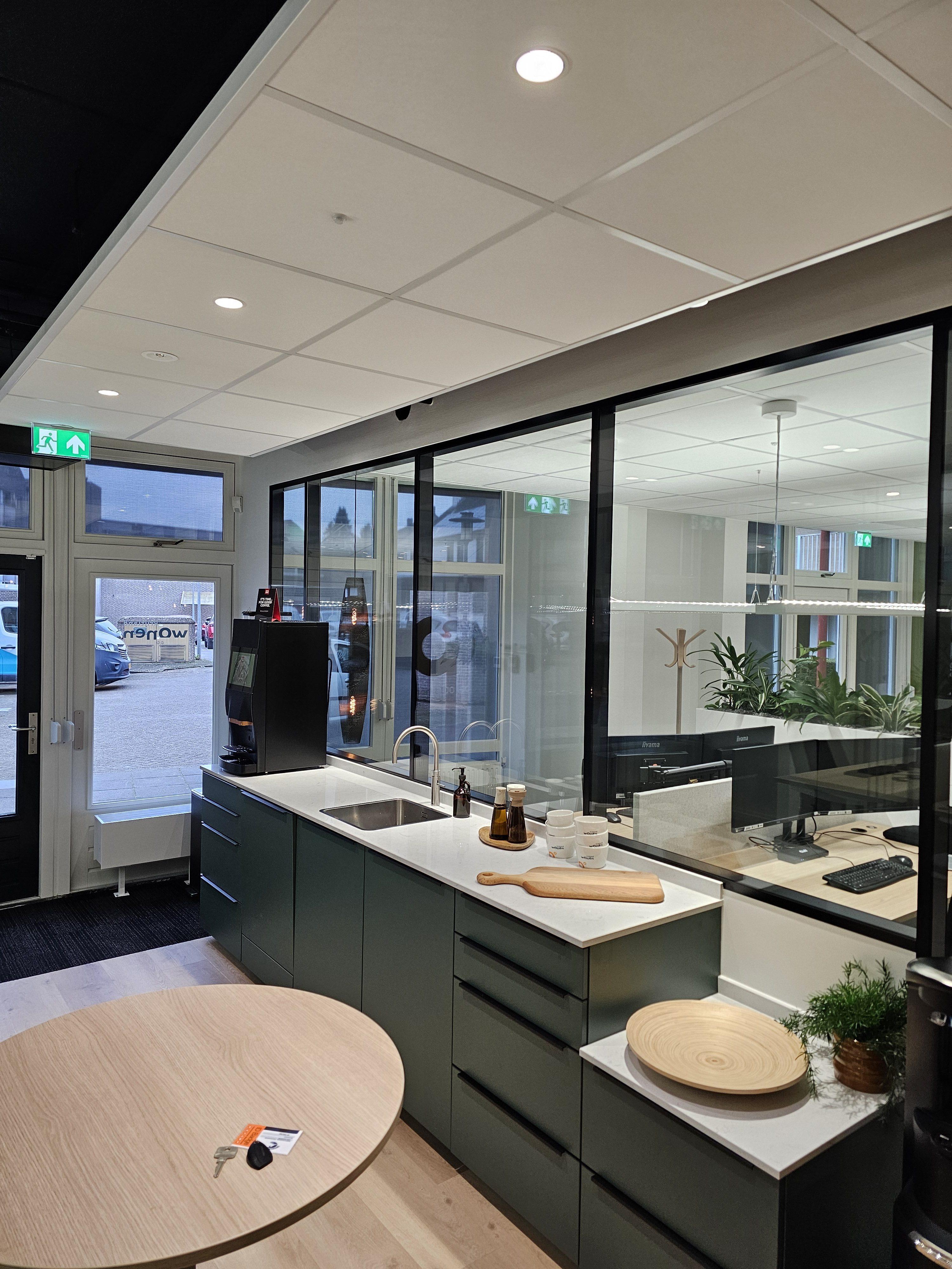 Een moderne keuken met op de achtergrond een kantoorruimte waarin bureaus met verschillende computers staan