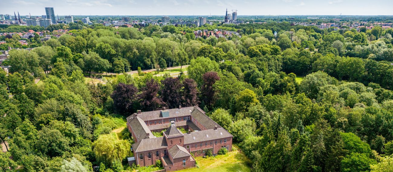 Luchtfoto van een woning omringd door veel groen met een stad in de verte.