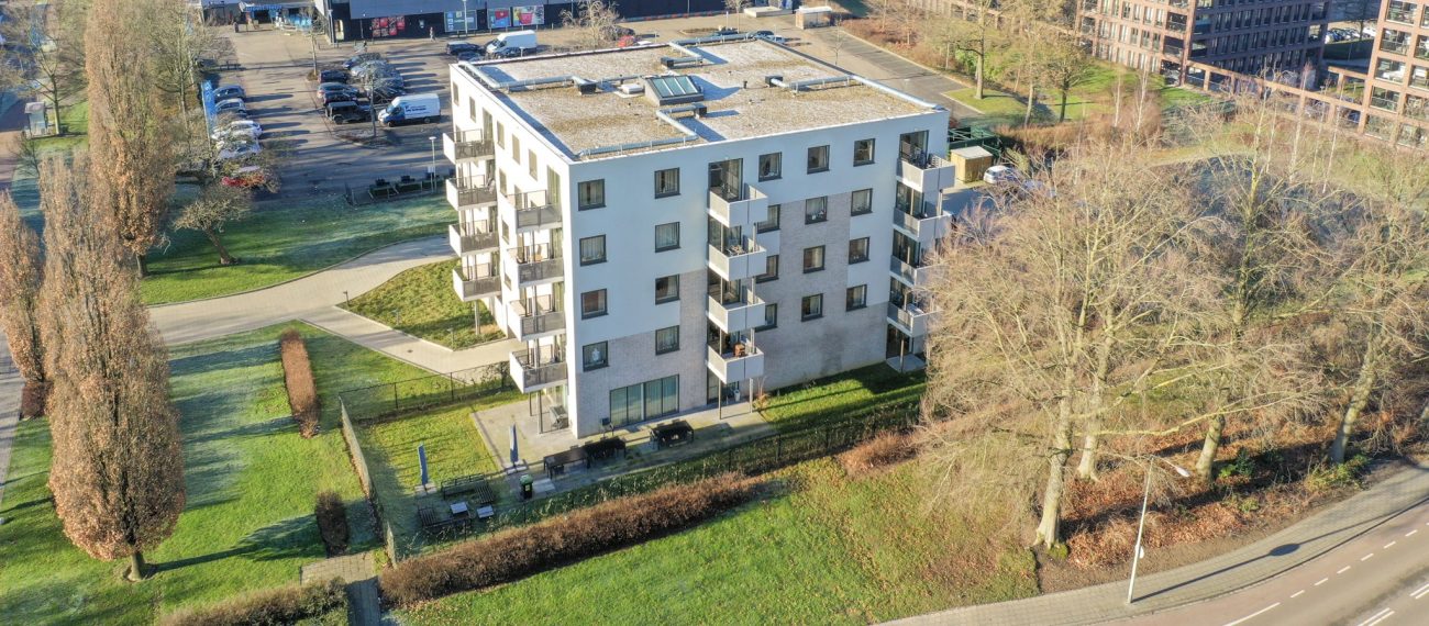 Luchtfoto nieuwbouw Noorderkroon Brunssum – vijflaags appartementengebouw met balkons en plat dak, gelegen naast winkelcentrum en hoogbouw in groen stadsdeel