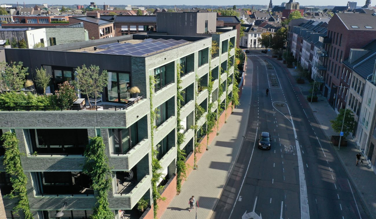 CPO Sphinx Maastricht – groene baksteengevel met verticale klimplanten en loggia’s, dakterras met zonnepanelen langs stadsstraat