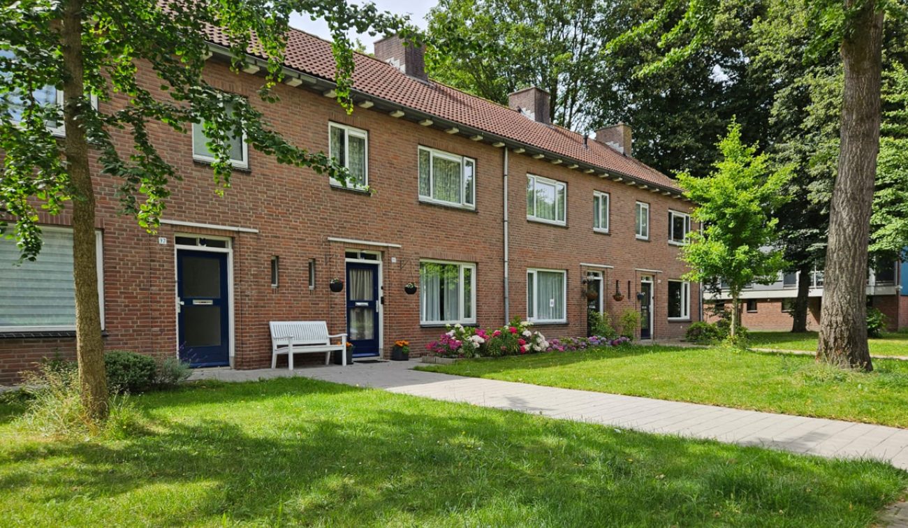Straatbeeld van het Bernadusplein in Tilburg met groen en woningen op de voorgrond, vastgelegd tijdens het groot onderhoudsproject.