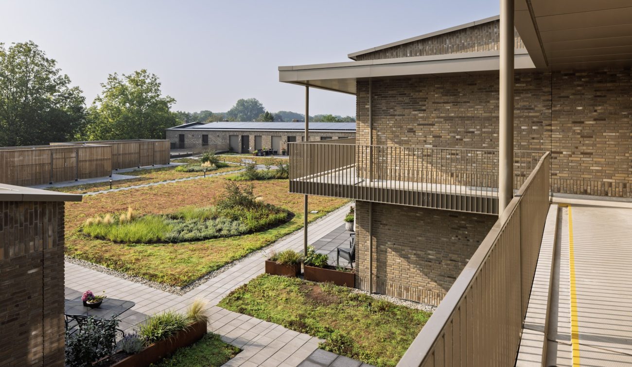 De Scheperij Teteringen: binnenhof met galerijbalkons, baksteen, wadi-tuin, paden en groen uitzicht.