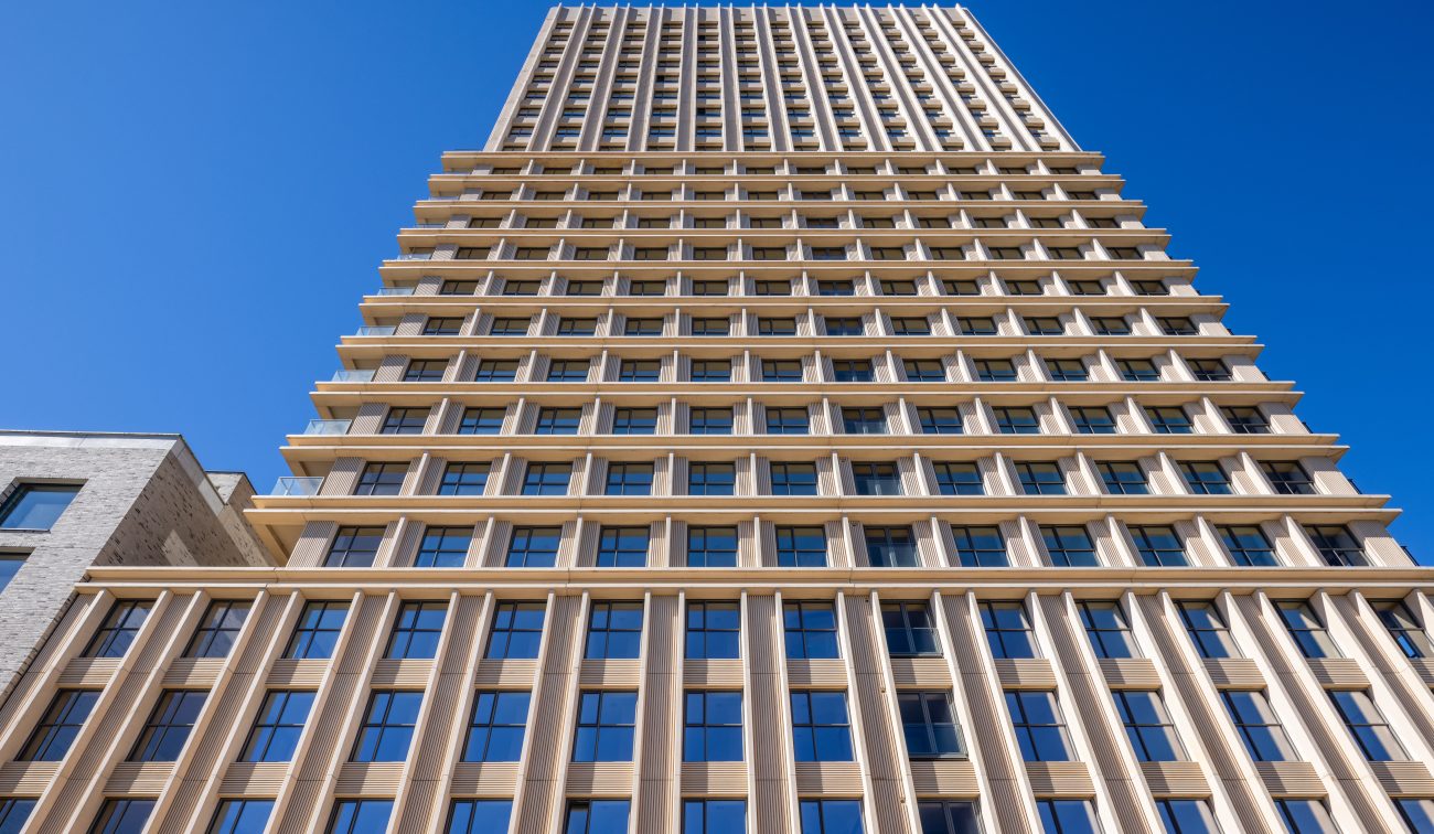 Ontwikkeling De Bankier Tilburg – close-up omhoogkijkend perspectief van de toren met ritmische geveldetaillering en grote raamvlakken tegen een helderblauwe lucht.