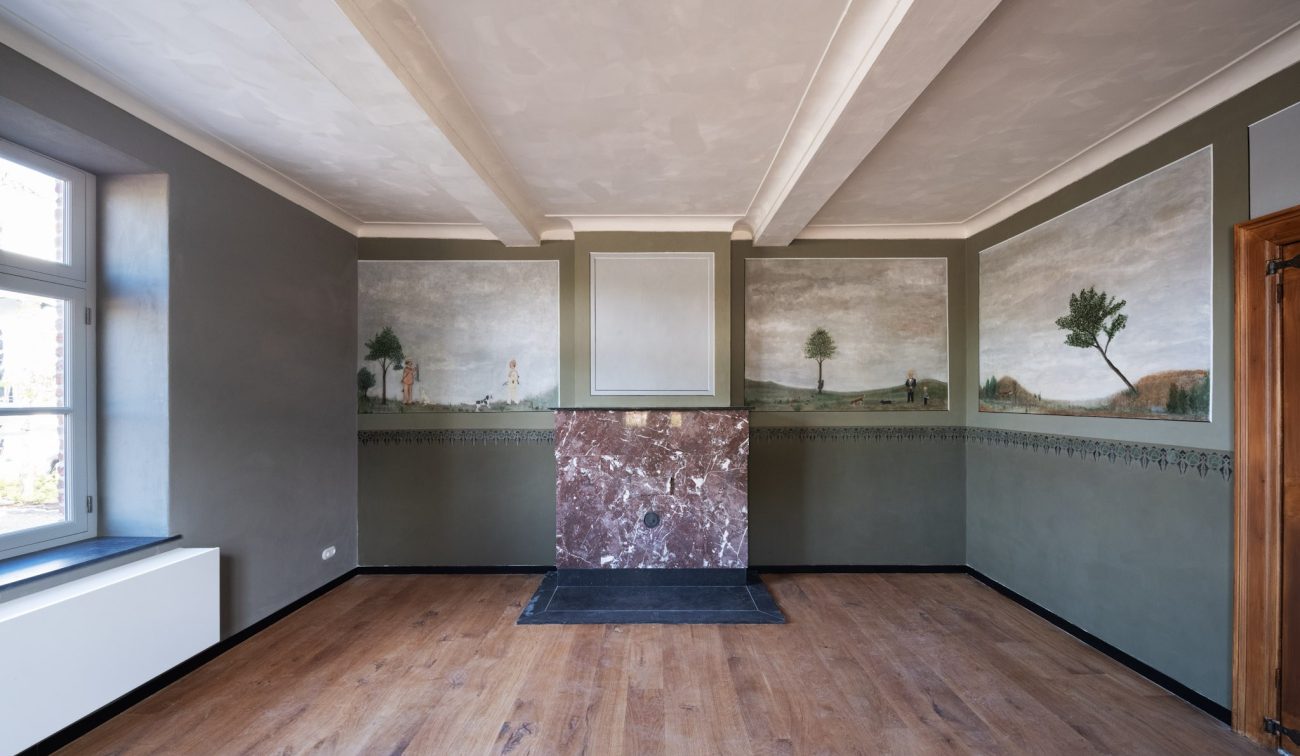 Gerestaureerde kamer in de Grathemermolen met houten vloer, donkergroene wanden met landschappelijke muurschilderingen en een centrale marmeren schouw.