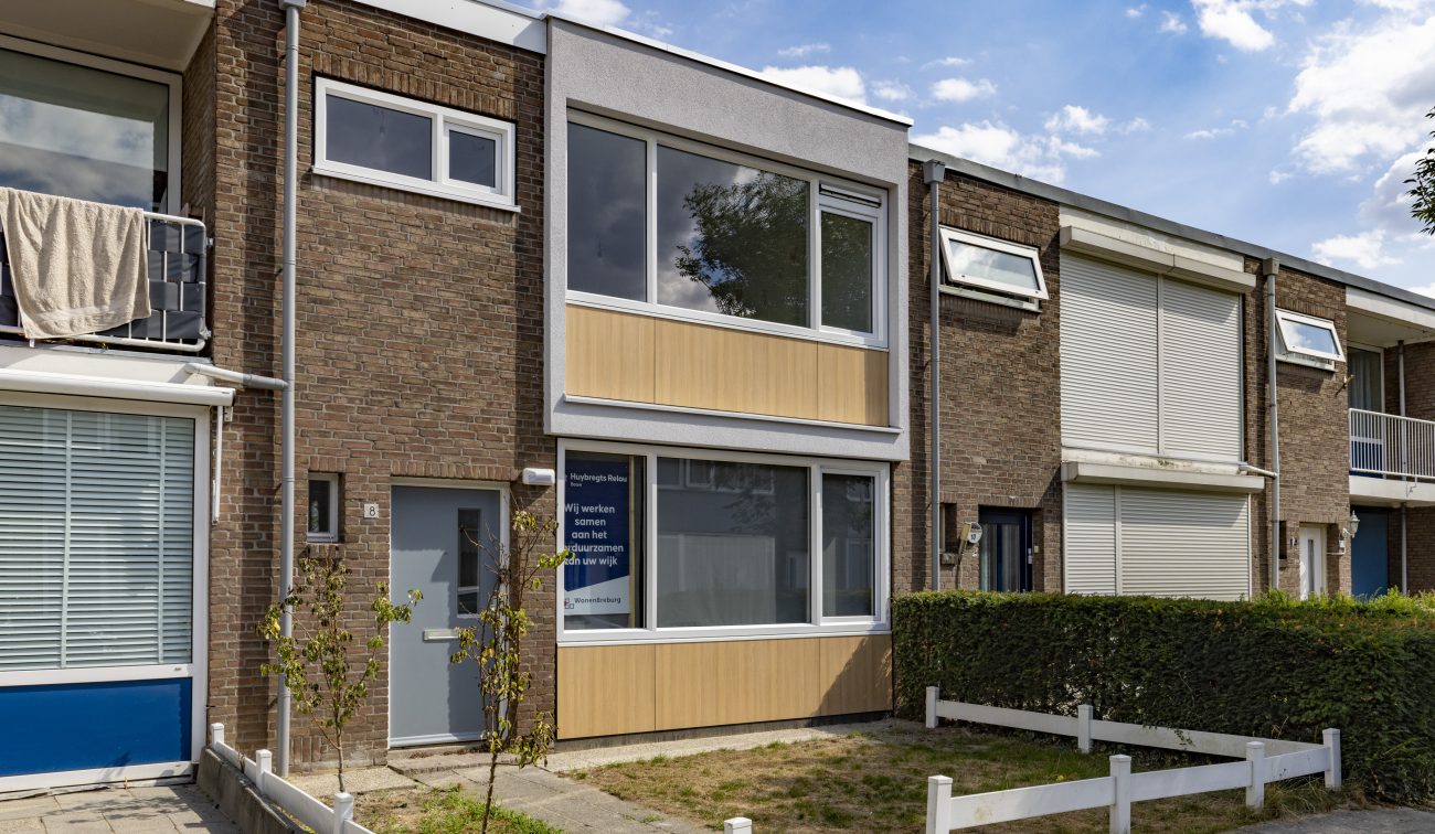 Groot onderhoud Staatsliedenbuurt Tilburg – rijwoning met vernieuwde voorgevel, isolerende gevelpanelen in houtlook en wit kader, nieuwe kozijnen en groot raam, tussen bestaande woningen.