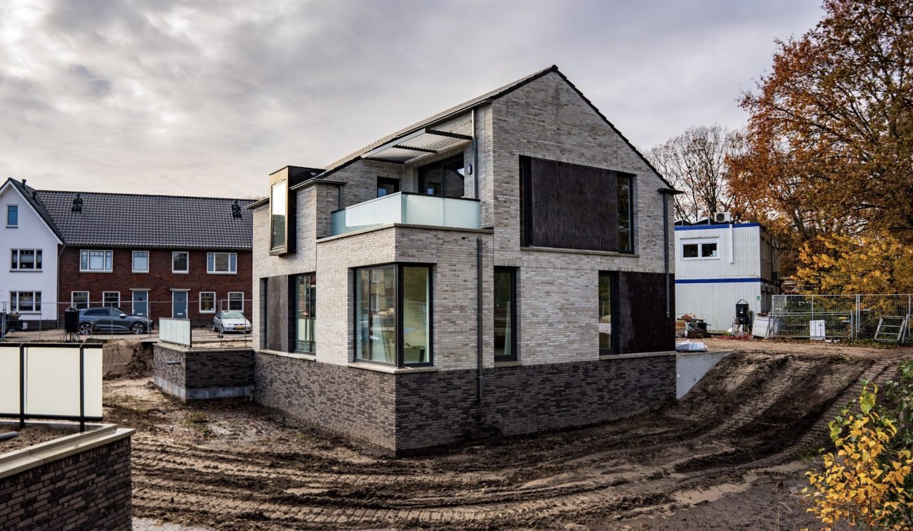Beeld van een moderne nieuwbouwwoning in het project Wilhelminahaven in Oosterhout, met lichte gevelstenen, glazen balkon en omliggende bouwlocatie.