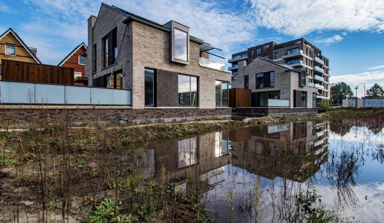 Beeld van het nieuwbouwproject Wilhelminahaven in Oosterhout, met moderne woningen en appartementen aan het water, weerspiegeld in de vijver.
