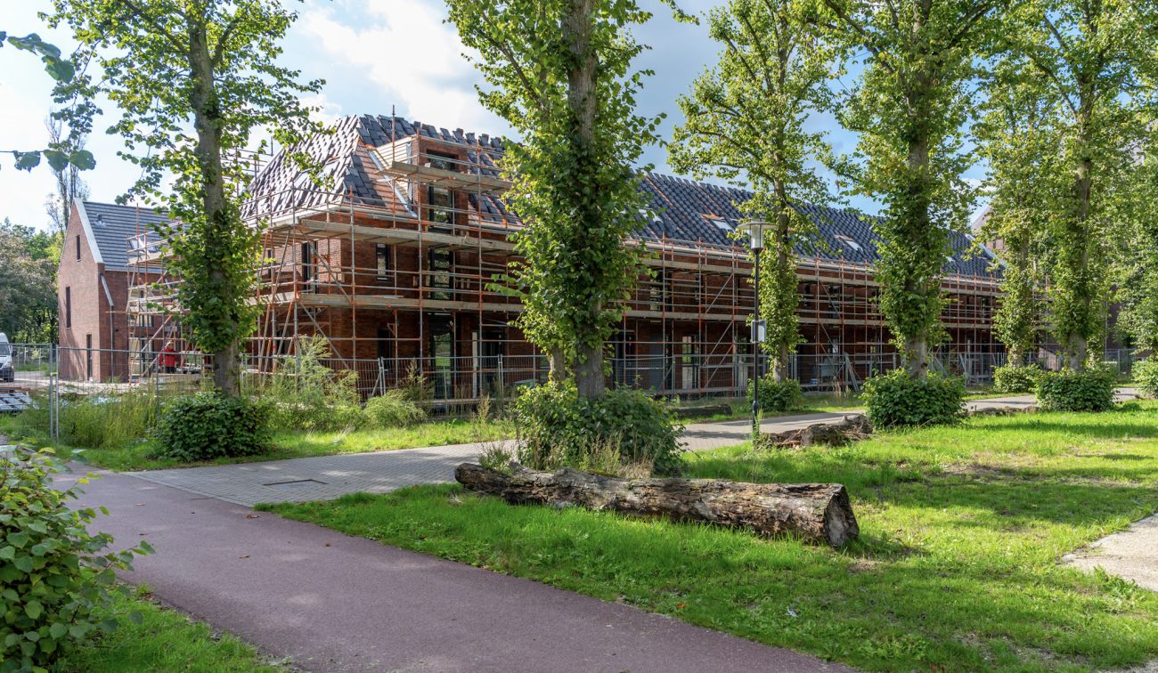 Kloostervelden Sterksel – rijwoningen in rood baksteen met steigers en dakpannen in aanleg, langs groene laan met fietspad en bomen