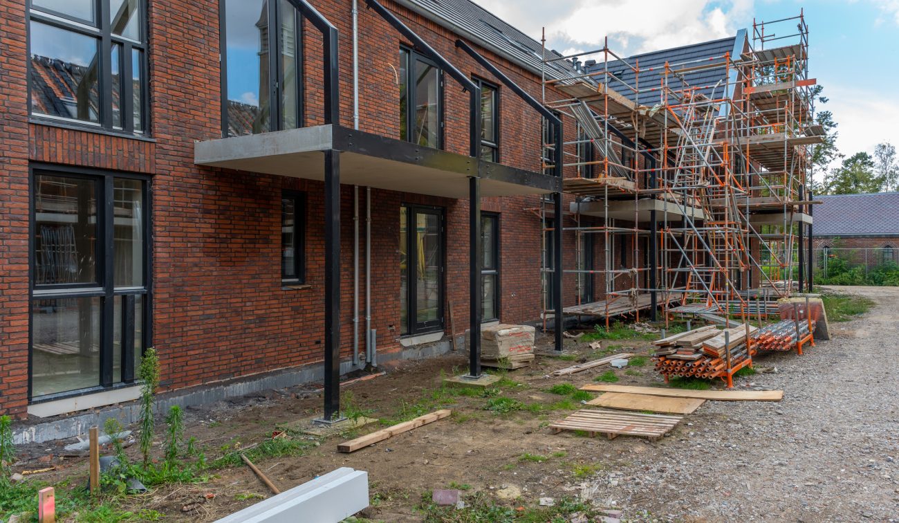 Kloostervelden Sterksel – rijwoningen in rood baksteen met stalen balkonconstructies in aanbouw, steigers en bouwmateriaal op erf