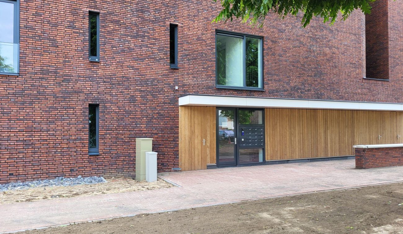Entree nieuwbouw sociale huurappartementen Margraten met houten geveldelen en brievenbussen.