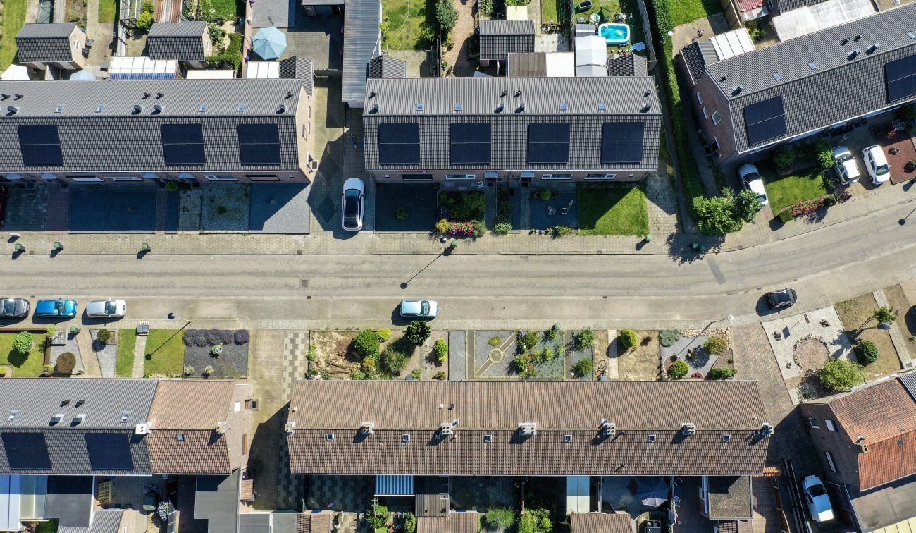 Vogelvlucht van Nieuwdorp: rijtjeshuizen met donkere daken en pv-panelen langs rechte straat — Groot onderhoud 154 woningen Nieuwdorp Stein