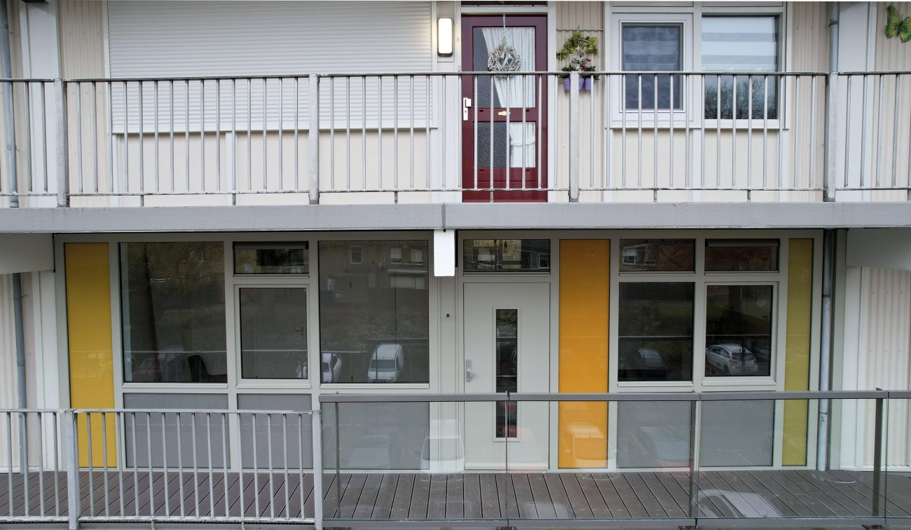 Galerijgevel met nieuwe kozijnen, glasdeur en gele accentpanelen achter metalen balustrade — Groot onderhoud Albert Schweitzer Brunssum
