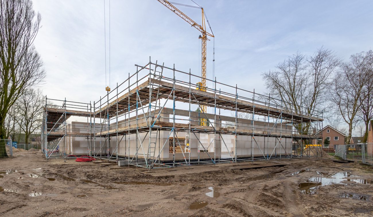 Nieuwbouw Antoniusschool Zundert: ruwbouw met steigers, kraan & betonwanden en modderig bouwterrein.