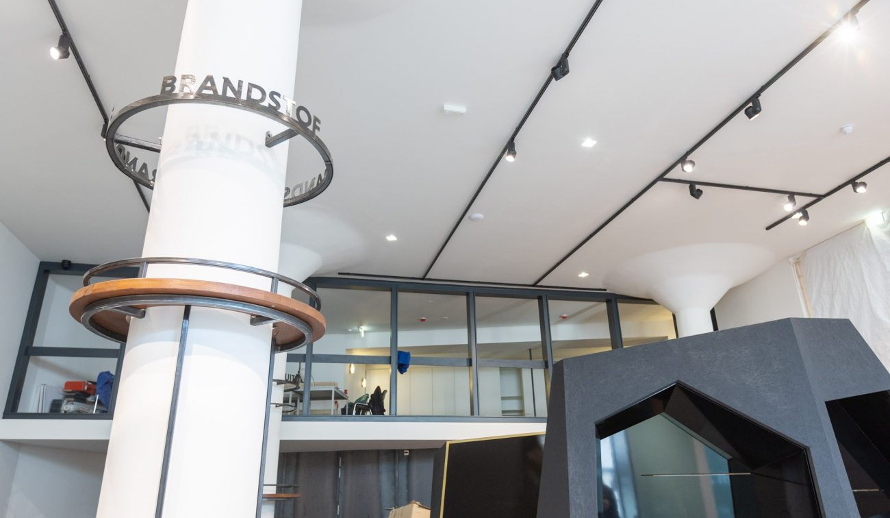 Interieur Nederlands Mijnmuseum met witte kolommen en zwarte railverlichting, glazen mezzanine en hoekige zwarte vitrine—opbouw van de tentoonstelling.