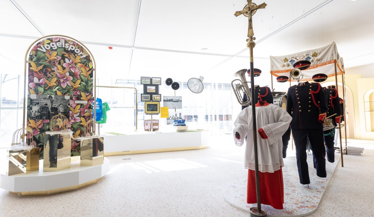 Expositie in het Nederlands Mijnmuseum met mannequins in fanfare-uniformen, blaasinstrumenten, vitrines en paneel ‘Vogelspot’ in een lichte zaal.