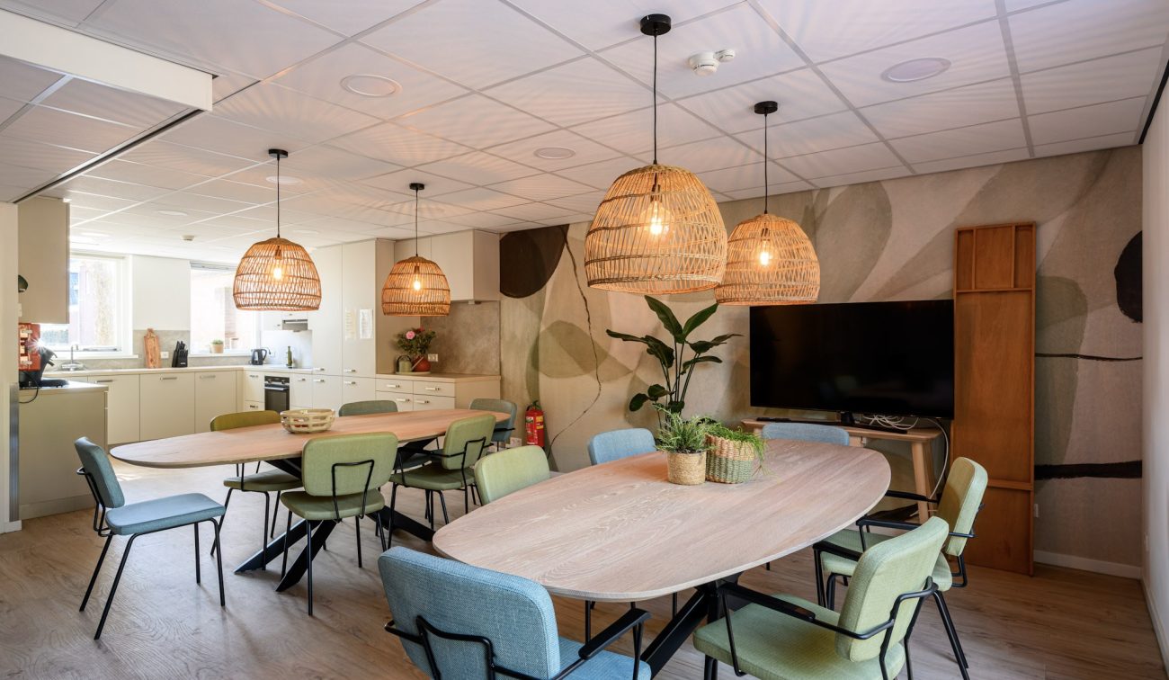Gezellige gemeenschappelijke ruimtes met ovale, houten tafels, rieten hanglampen, keuken en TV-hoek.