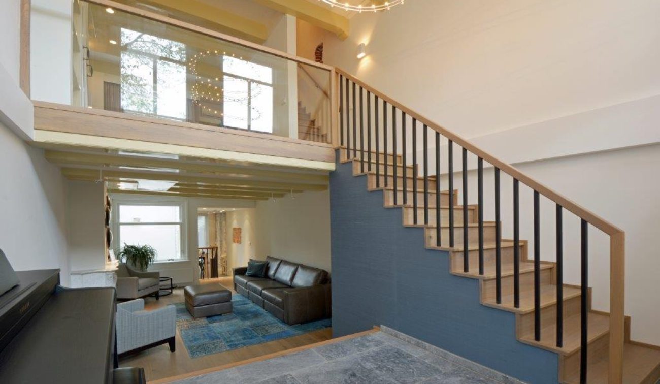Renovatie Egelantiersgracht Amsterdam: woonkamer met vide, houten trap met stalen spijlen en glasbalustrade