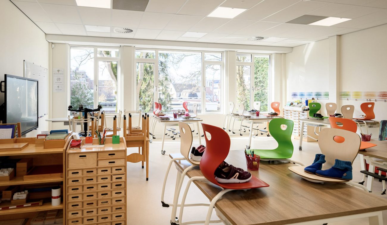 Renovatie Kindcentrum LEF Utrecht – licht klaslokaal met grote ramen, flexibele werkplekken en kleurrijke, ergonomische stoelen; praktische opbergmeubels en roltafels ondersteunen verschillende lesvormen.