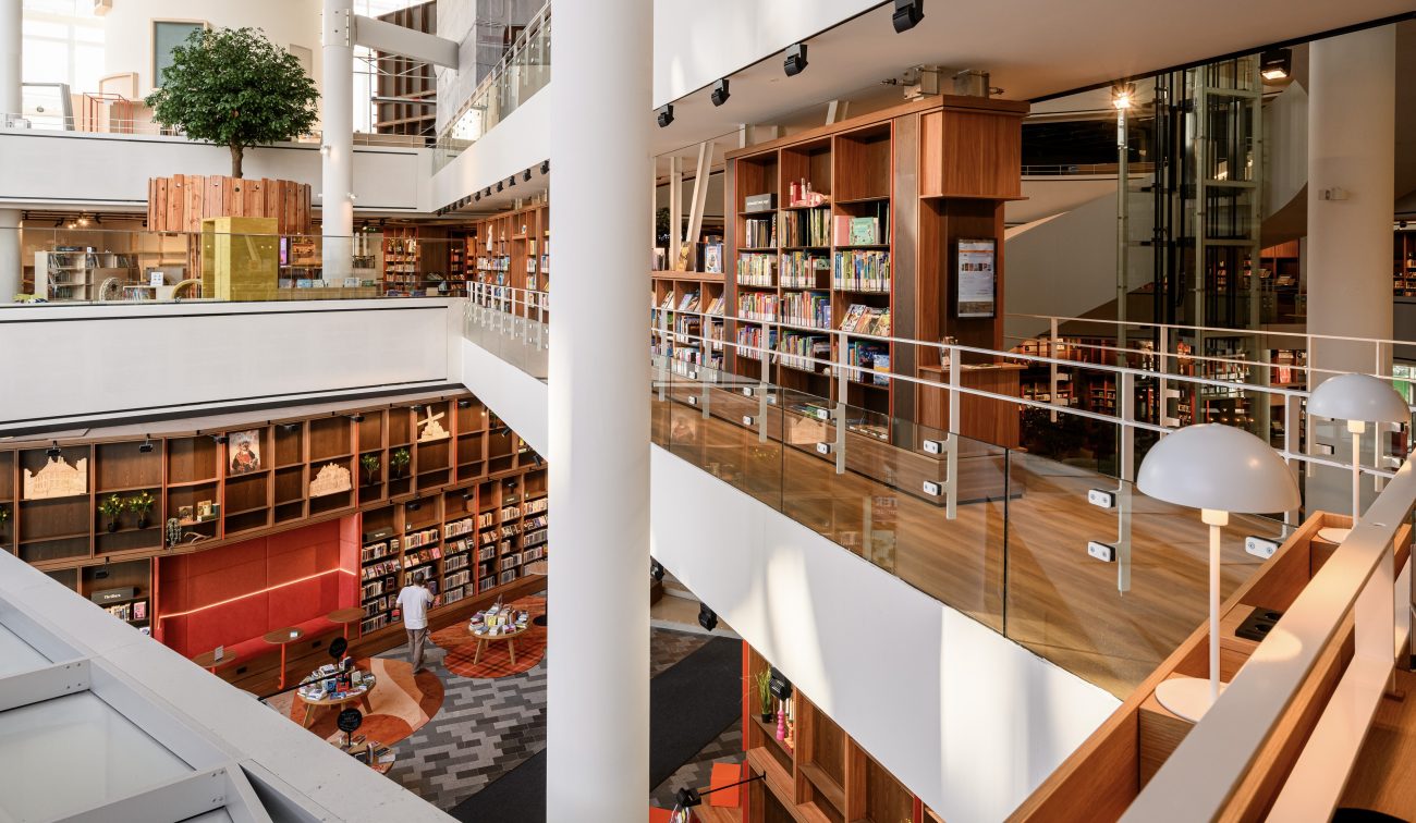 Lichte atriumbibliotheek met houten boekenkasten, glazen balustrades en witte kolommen.