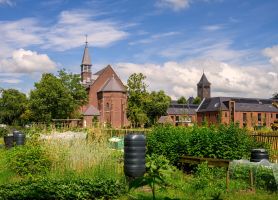 Klooster en nieuwbouwwoningen in Kloostervelden in Sterksel met zonnepanelen op de daken en een groene moestuin op de voorgrond.