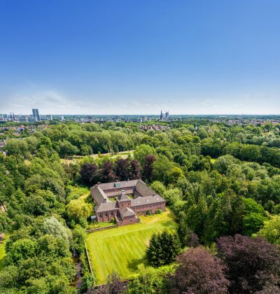 Luchtfoto van een woning omringd door veel groen met een stad in de verte.