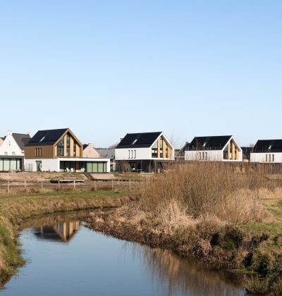 Nieuwbouwwoningen langs watergang met rietoevers in groene woonomgeving