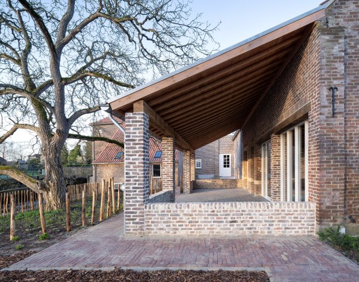 Overdekte veranda met houten spanten en bakstenen kolommen aan de Grathemermolen in Grathem, met metselwerkgevel, grote schuiframen en bestrate voorruimte.