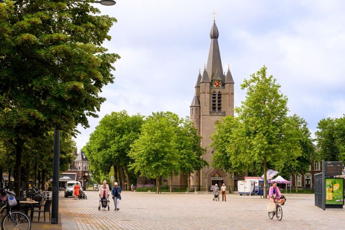 Valkenswaard – Markt met monumentale kerk, groene platanen en mensen die lopen en fietsen op het plein.