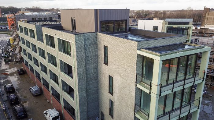 CPO Sphinx Maastricht – groene baksteengevel met grote raamkaders en glazen balkons, bouwterrein met busjes zichtbaar