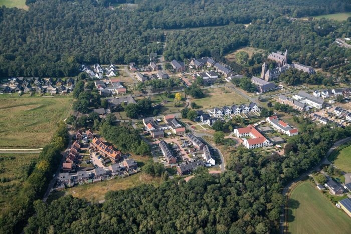Kloostervelden Sterksel – luchtfoto van woonwijk rond kloostercomplex met kerktorens, rijwoningen en vrijstaande huizen aan de bosrand