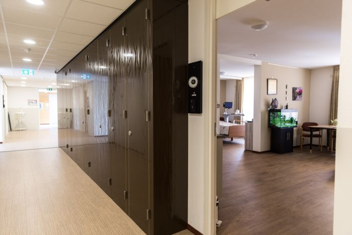 Gang woonzorgcentrum Beukeloord met glanzende kastenwand en doorkijk naar zorgkamer met aquarium.