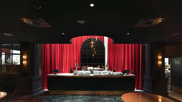 Foyerbalie met rode fluwelen gordijnen, boogvormige spiegel en hanglampen in een donker interieur.