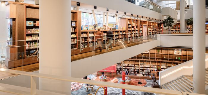 Meerdere verdiepingen met houten boekenkasten, glazen balustrades en brede trap in bibliotheek.