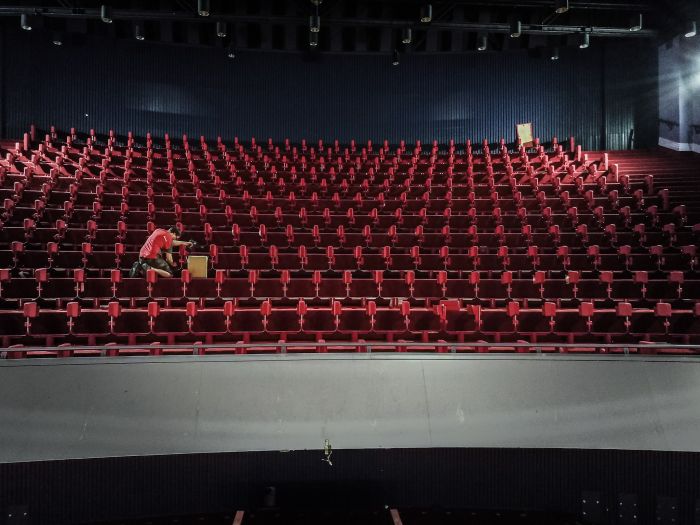 Montage in grote zaal: technicus werkt tussen rijen rode stoelconstructies tijdens verbouwing
